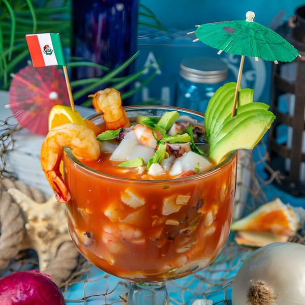 Mexican seafood cocktail with shrimp, octopus, and avocado, garnished with a Mexican flag and umbrella.