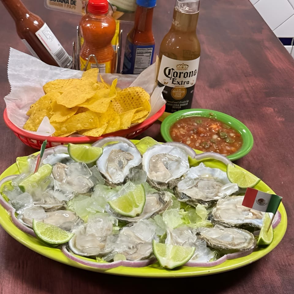 Fresh oysters on ice with lime, tortilla chips, salsa, hot sauce, and a Corona beer.