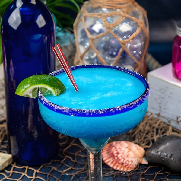 A vibrant blue El Dorado Mexican Restaurant margarita with a lime wedge and red straws.