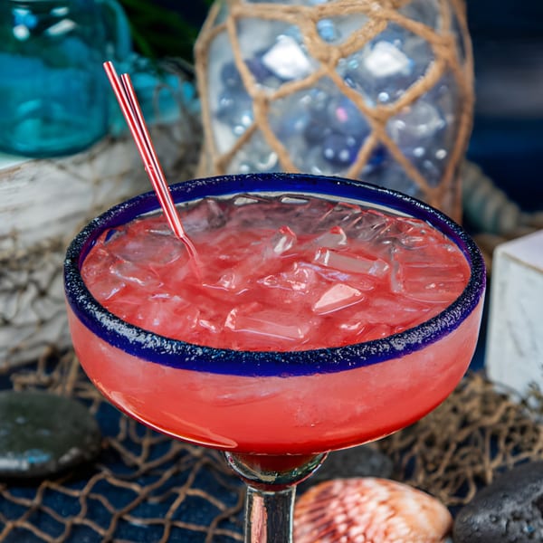 A vibrant red margarita with ice and two red straws, in a blue-rimmed glass, on a nautical background.